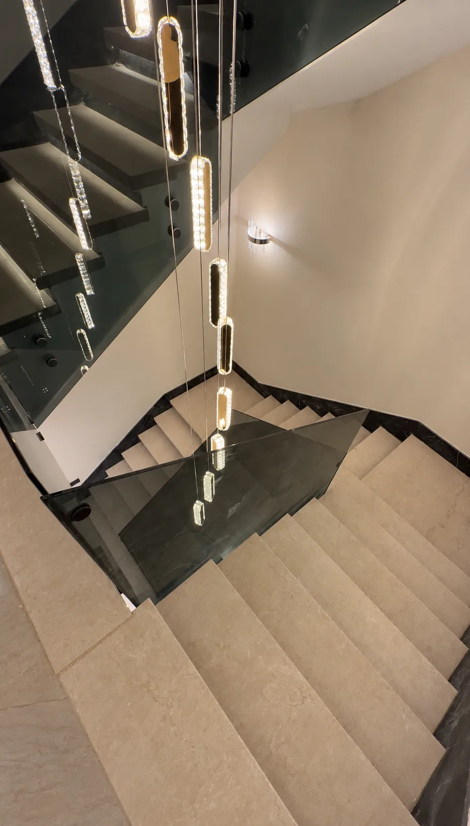 Looking down the stairwell past the chandelier and the glass balustrade.
