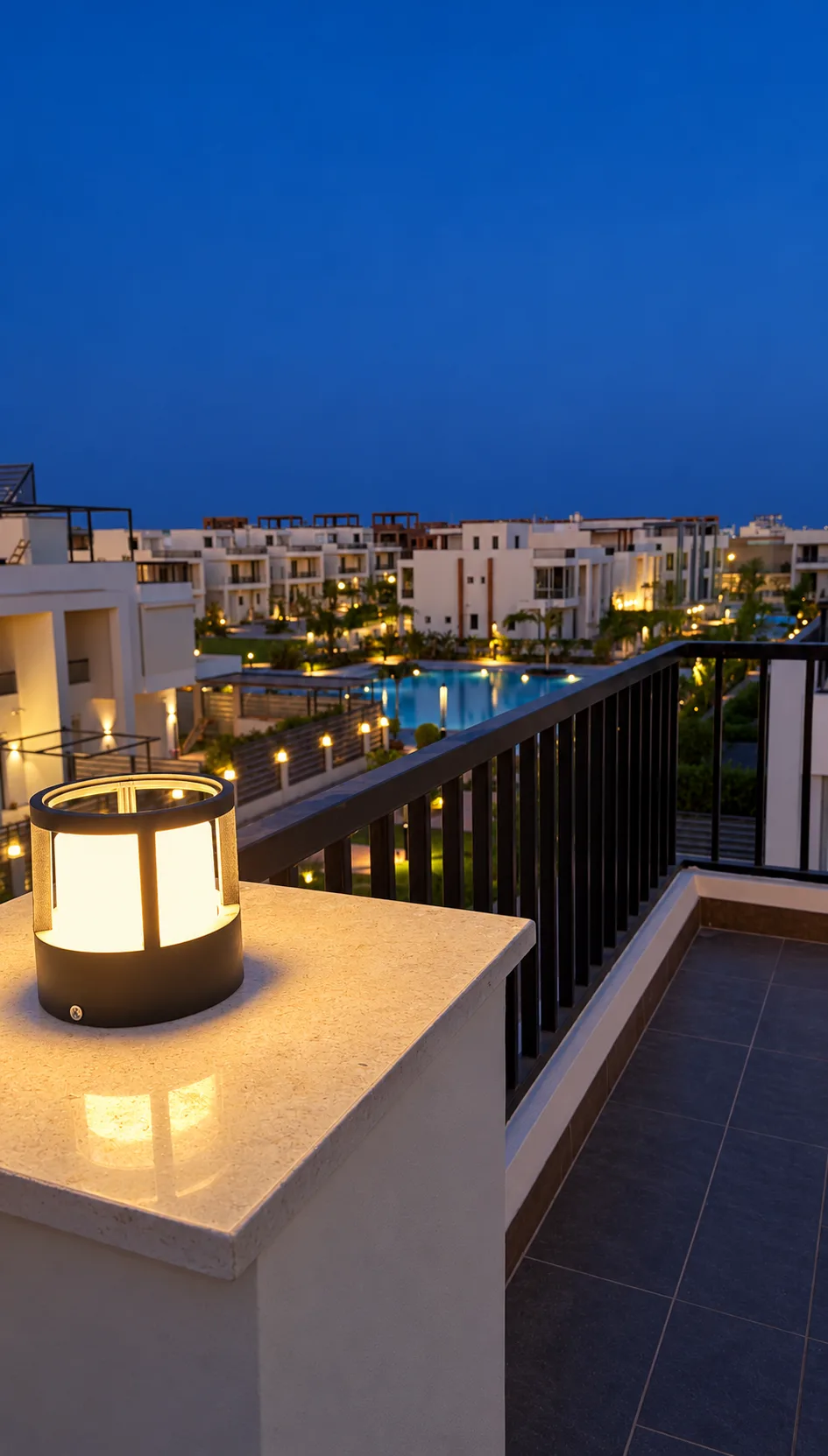The terrace at dusk: a lit lantern on the parapet, a black railing and the lights of the neighbourhood beyond.