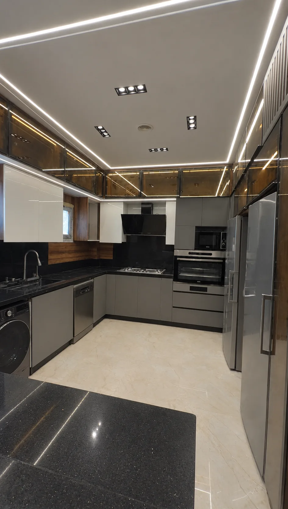 The kitchen seen from the end of the island: grey cabinets, built-in ovens and lit cabinets along the ceiling.