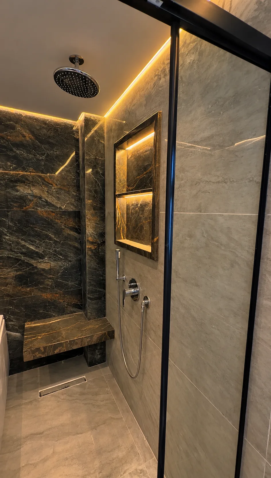 The walk-in shower of the same bathroom: a rain shower, a stone bench and a lit niche.