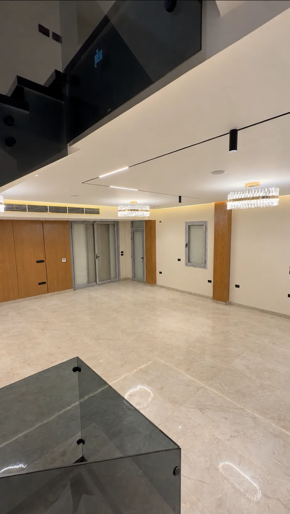 The reception hall seen past the glass balustrade of the stairs: a wood-clad wall, chandeliers and cove lighting.